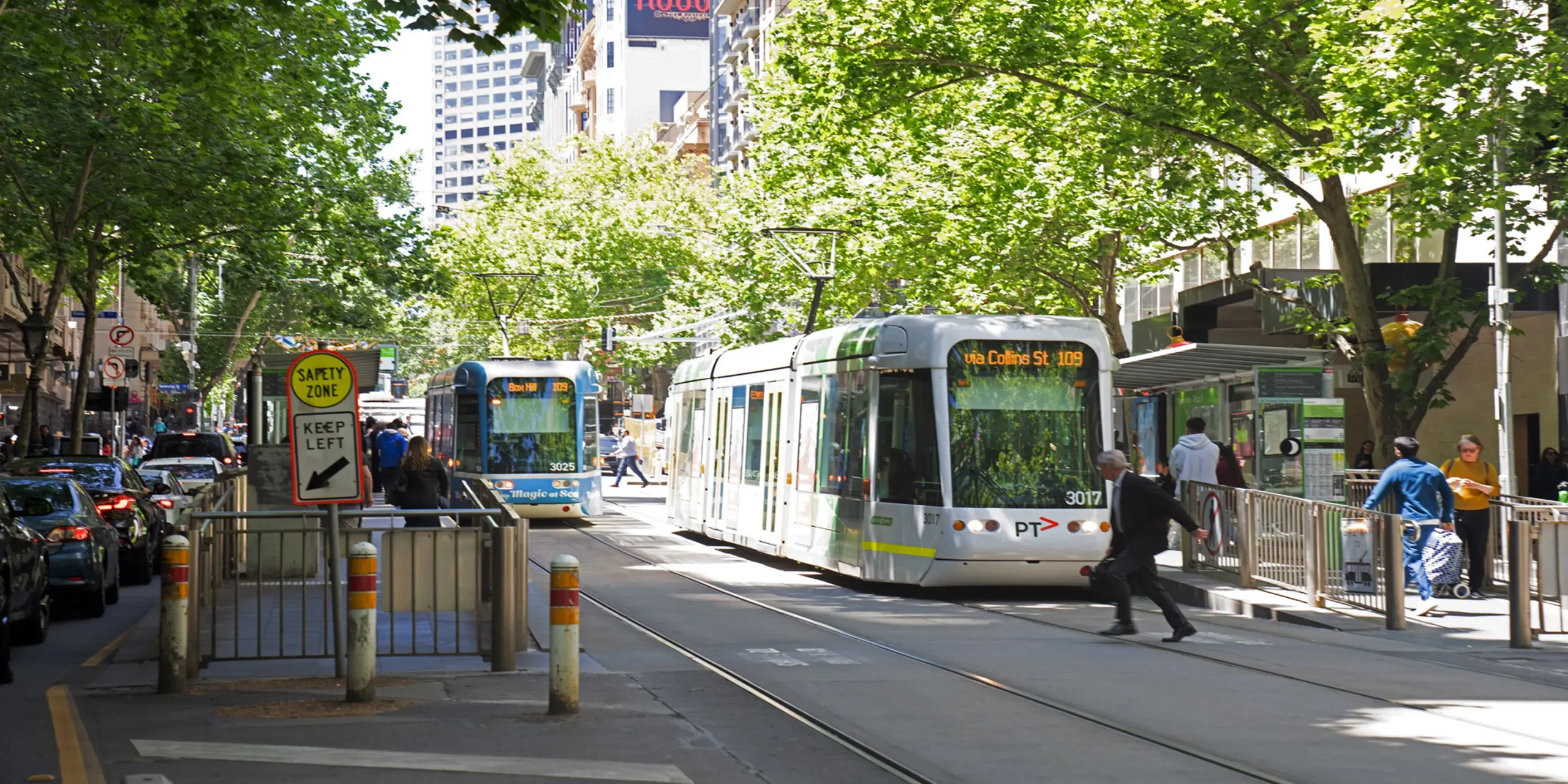 An image of Melbourne's Town Hall tram stop on Collins St on a sunny day, Trams stopping on either side to pick up passengers in the free tram zone.