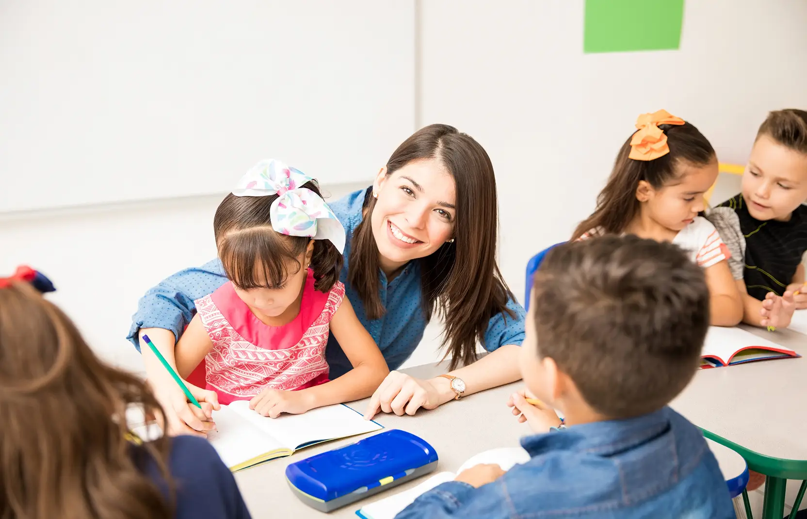 An early childhood teacher helping their students write in a notebook.